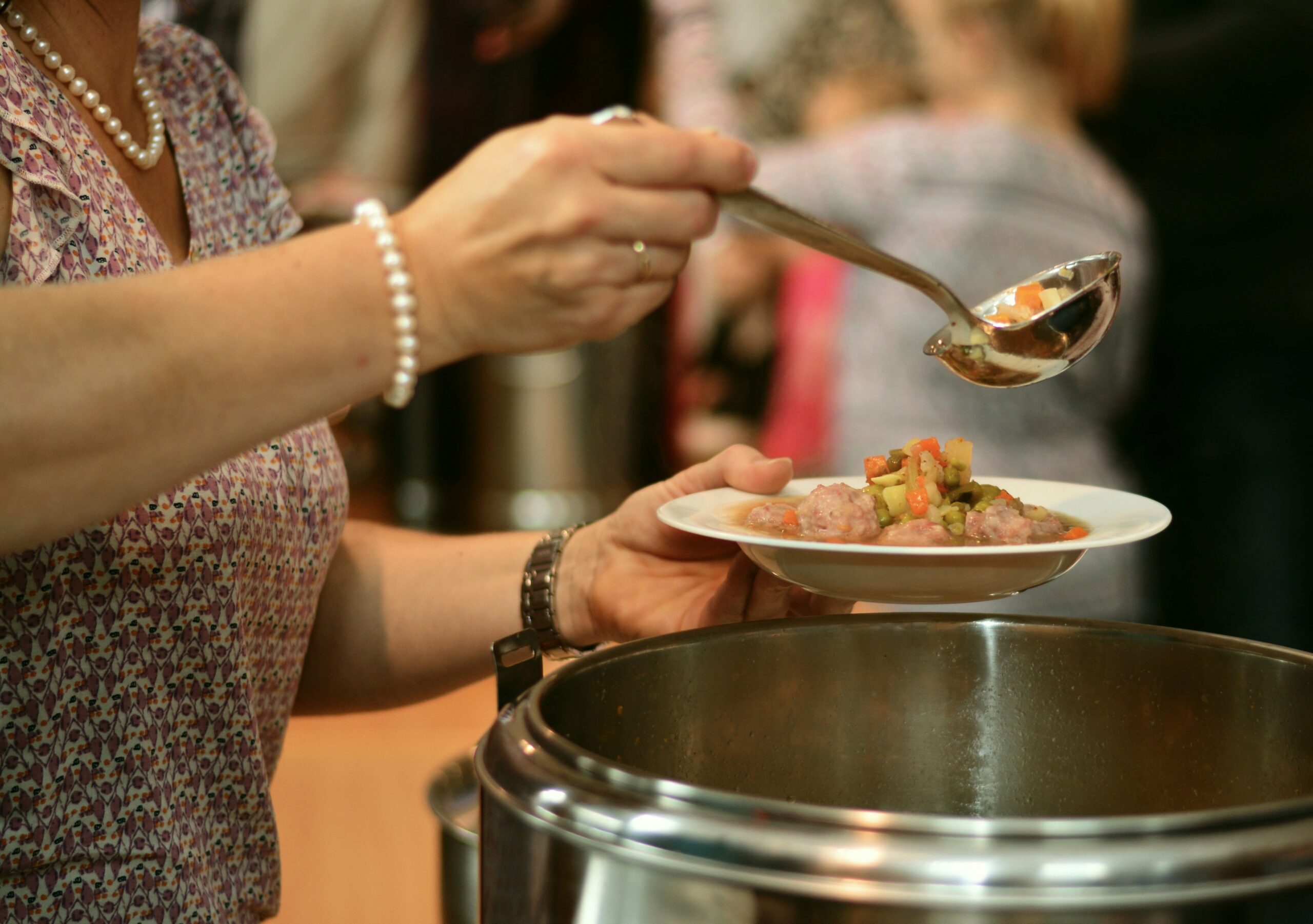 A person serving food at a community meal, representing food systems, cultural programming and support for a growing social enterprise.